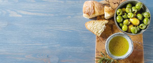 Olivier oil with fresh herbs and bread. Blue background. Italian and Greek national food. Top view